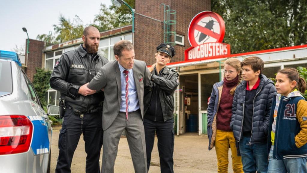 Geschäftsmann Lackmann (Oliver Sauer) wird von zwei Polizisten festgenommen. Pinja (Sina Michel), Ramin (Jann Piet) und Jale (Ava Sophie Richter) stehen daneben.