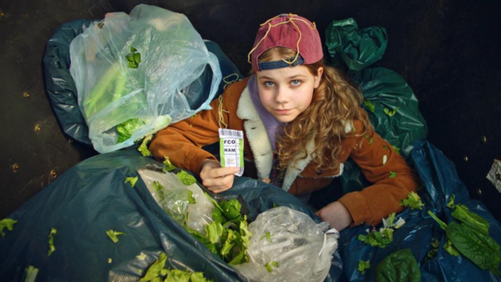 Malin sitzt in einem Müllcontainer, umgeben von Küchenabfällen.