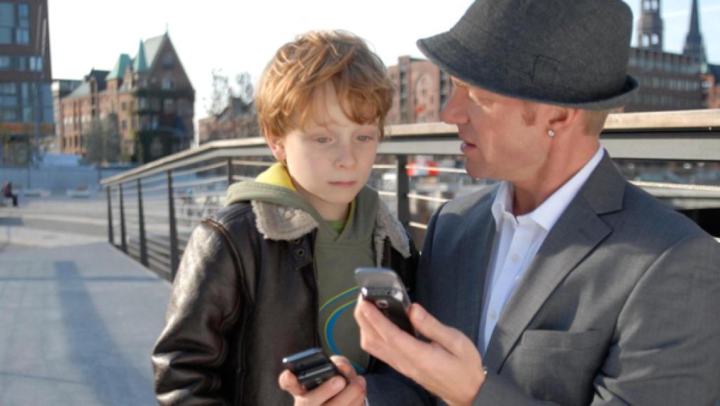Ein Mann mit Hut zeigt Henri etwas auf dem Handy