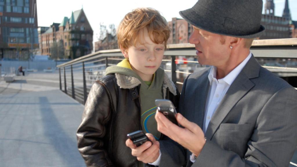 Ein Mann mit Hut zeigt Henri etwas auf dem Handy