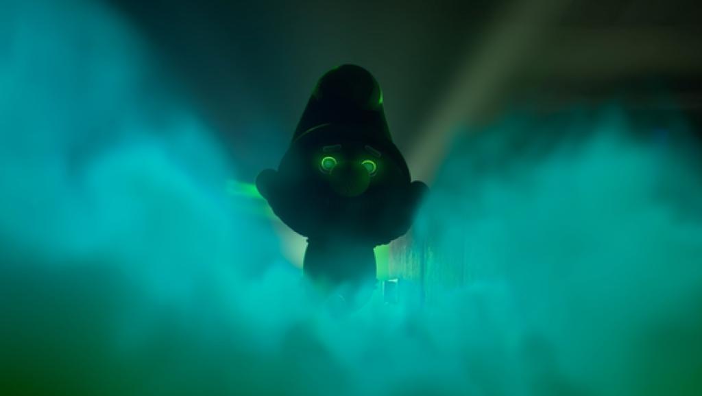 In einer dunklen, grünlich leuchtenden Wolke steht ein geheimnisvoller Schlumpf mit grünen Augen.