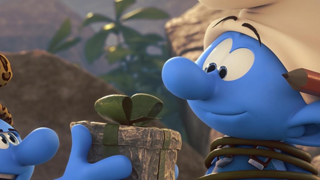 Handy ist an einen Pfahl gefesselt. Vor ihm steht ein Steinzeit Jokey und hält ihm ein Paket hin.