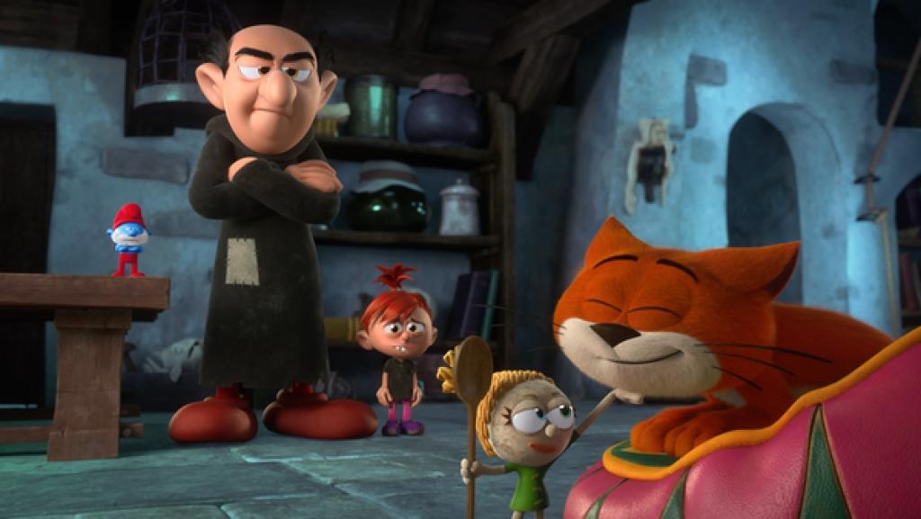 Eine Stoffpuppe hat in der einen Hand einen Kochlöffel, mit der anderen krault sie eine orangen-farbene Katze. Gargamel und Rowena stehen verwundert daneben.