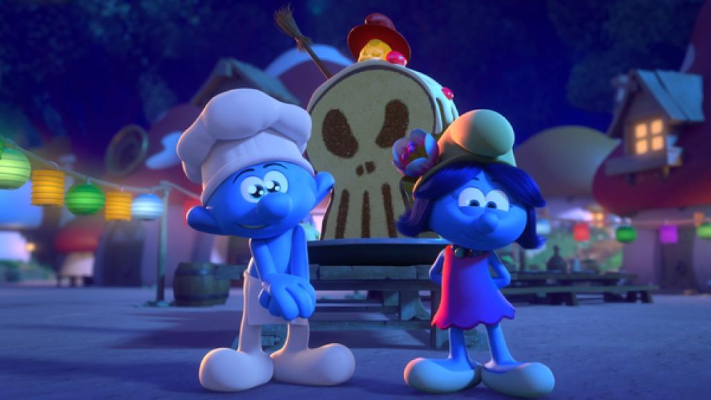 Vor einem Kuchen in Totenkopf-Form stehen Koch-Schlumpf und eine Schlumpfin mit glänzenden Augen.