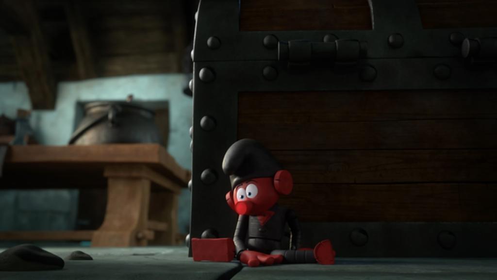 Eine rote Schlumpf-Holzpuppe mit schwarzer Mütze sitzt ungelenk und leblos am Boden hinter einer Truhe.