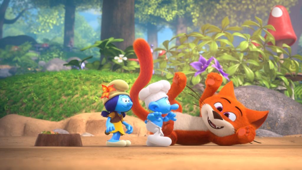 Lily und Koch stehen lächelnd vor einer jungen, orangefarbenen Katze, die verspielt am Boden liegt.