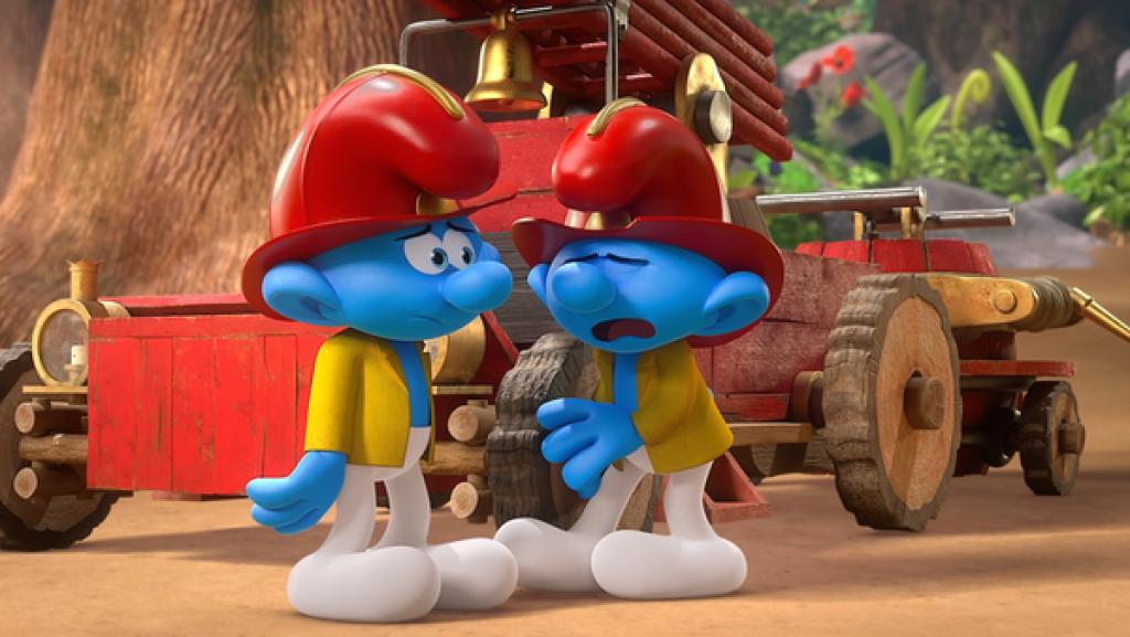 Zwei Schlümpfe mit roten Feuerwehrhelmen und gelben Jacken stehen im Wald vor einem roten Feuerwehrauto. Sie schauen etwas unglücklich.