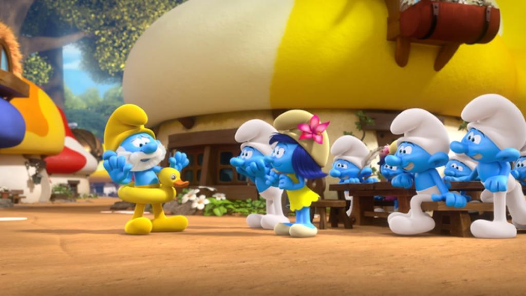 Papa Schlumpf trägt ein gelbes Outfit mir einem gelben Enten-Schwimmreif um den Bauch. Einige Schlumpfe schauen begeisert zu ihm.