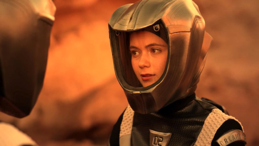 Emma, groß im Bild mit Raumanzug, draußen auf dem Mars, ist nachdenklich im Gespräch vertieft.