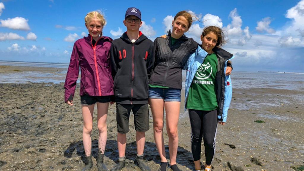 Vier Jugendliche stehen zusammen bei Ebbe im Watt.