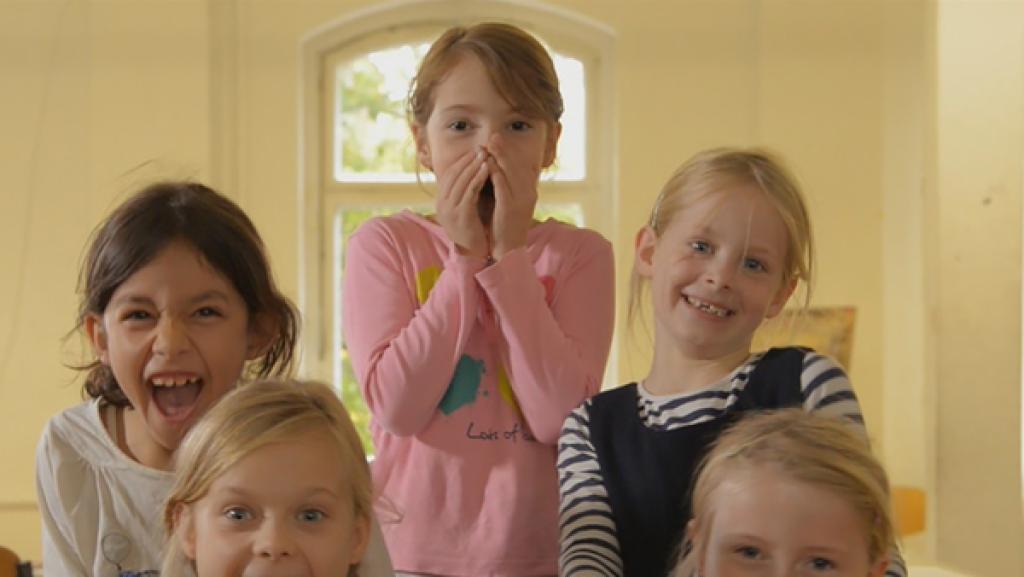 Fünf Mädchen stehen aufgereiht und lachen in die Kamera. Das mittlere Kind hält die Hände vors Gesicht.