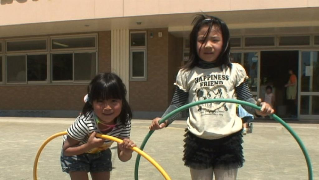 Zwei Mädchen stehen auf einem Hof und haben je einen Hula Hoop Reifen in der Hand.