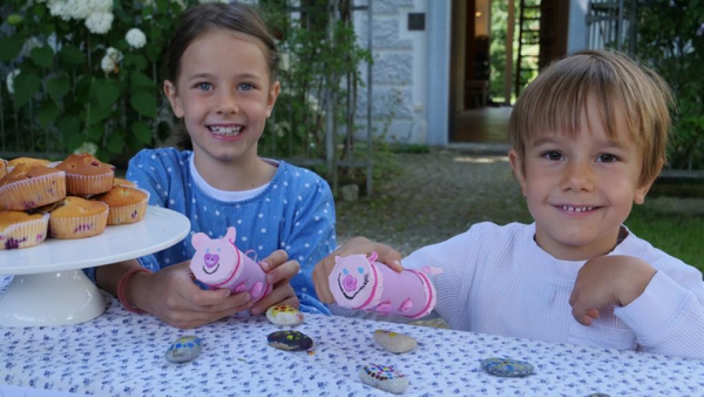 Zwei Kinder knien hinter einem Verkaufstisch, auf dem Muffins und angemalte Steine liegen.