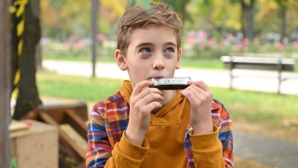 Mats spielt mit einer Mundharmonika und schaut in die Ferne.