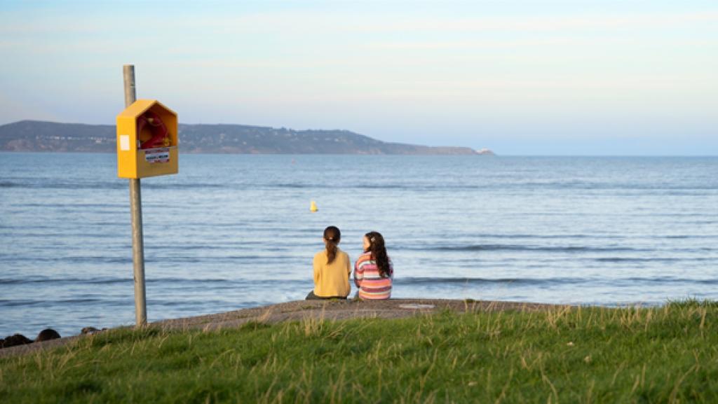 Yana und Chloe sitzen am Ufer und schauen auf das Meer.