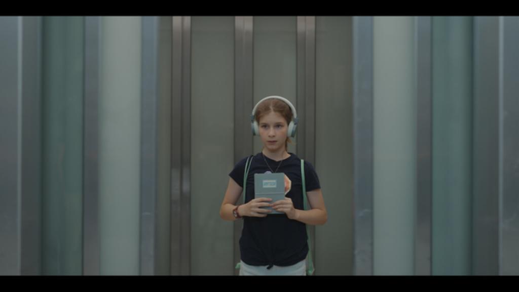 Rechte: KiKA/eitelsonnenschein GmbH Eileen steht alleine in einem großen Fahrstuhl in einem Einkaufszentrum. Sie trägt ihre Kopfhörer.