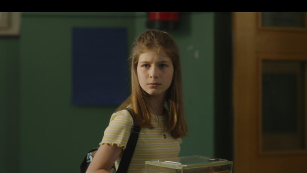 Rechte: KiKA/eitelsonnenschein GmbH Eileen steht im Schulflur und hält ihr Formicarium in den Händen. Darin lebt ihr Ameisenstaat.