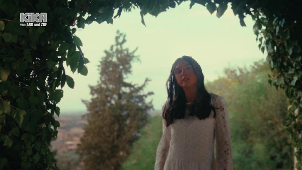 Inês Gonçalves steht im weißen Kleid eingerahmt von einem Bogen aus Blättern.