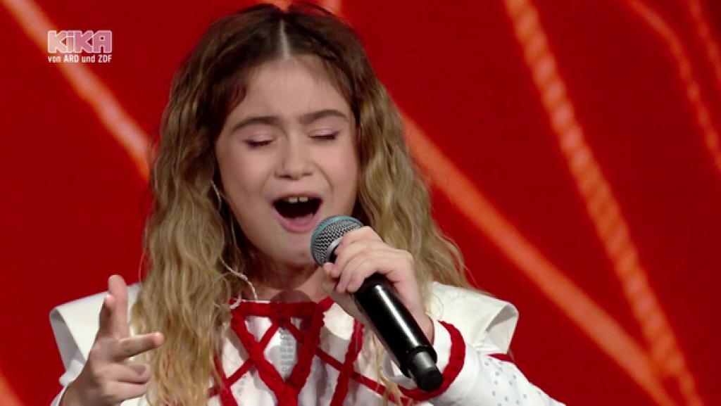 Sofia Nersesian singt in ein Mikrofon. Sie trägt ein weiß-rotes Outfit.