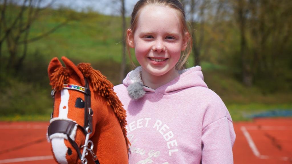 Rechte: KiKA/Franziska Gruber Die zwölfjährige Emily ist ein Riesenfan von Hobby Horsing. Sie trägt einen rosa Kapuzenpullover und hält das Steckenpferd in der Hand.