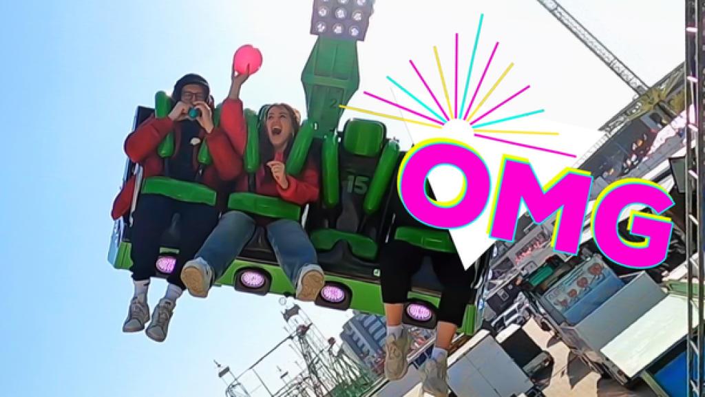 Rechte: KiKA/Rozhyar Zolfaghari Auf einem Sitz eines Fahrgeschäfts auf dem Hamburger Dom sitzen Ben (links) und Sarah. Rechts steht in pinker Schrift "OMG".