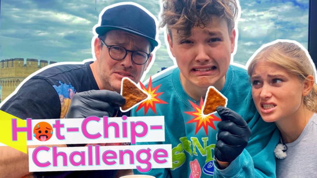 Rechte: KiKA/Sakina Gaba Eine Fotomontage. Links steht in pinken, fetten Buchstaben: "Hot-Chip-Challenge". Das "O" im Schriftzug ist mit einem roten, schwitzendem Emoji ersetzt. Mit Handschuhen halten HeyMoritz und Ben zwei sehr scharfe Chips vor die Kamera. Zoe sieht besorgt aus.