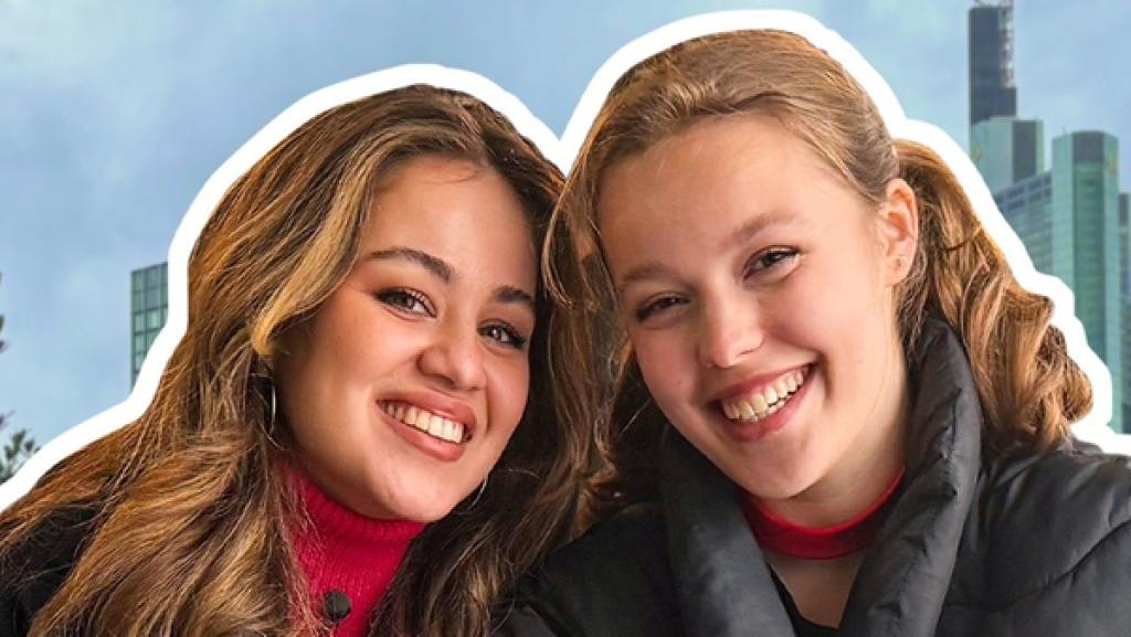 Rechte: KiKA/Antonia Hirnich Sarah und Emma-Josephine sitzen lächelnd eng nebeneinander an einem Tisch. Darauf liegen ein Schreibblock und Smartphones. Im Hintergrund die Frankfurter Skyline. Links unten die Aufschrift Ich schenke dir ein Gedicht.