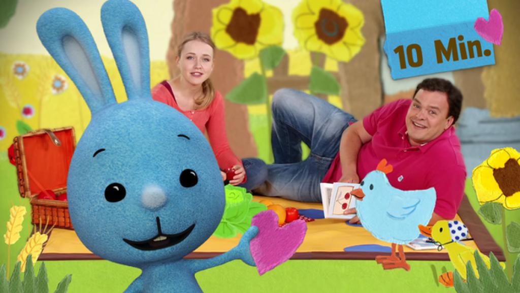 Kikaninchen hält ein Herz und ist mit Anni und Christian draußen beim Picknick.