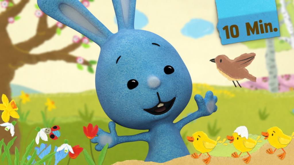 Kikaninchen steht lächelnd auf einer Frühlingswiese mit ausgebreiteten Armen.