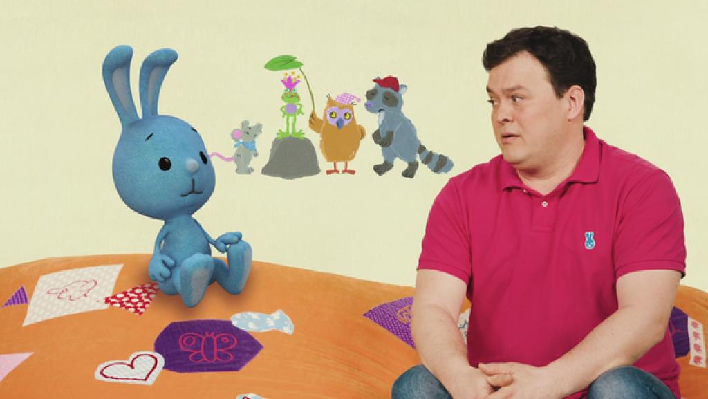 Kikaninchen und Christian sitzen auf einem orangen Kissen. Im Hintergrund sind viele Tiere.