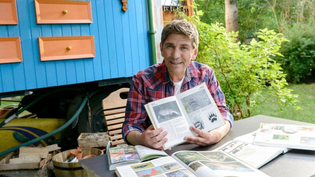 Fritz Fuchs sitzt vor dem Bauwagen mit einem Buch über Dachse