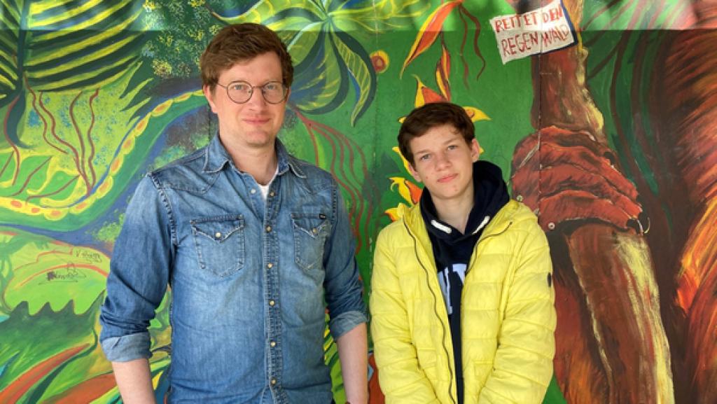 Robert und Jannis stehen vor einer bunt angemalten Wand in Jannis' Schule.