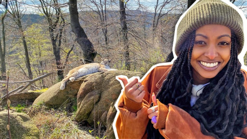 Reporterin Luam ist im Vordergrund und zeigt auf einen Luchs hinter ihr.