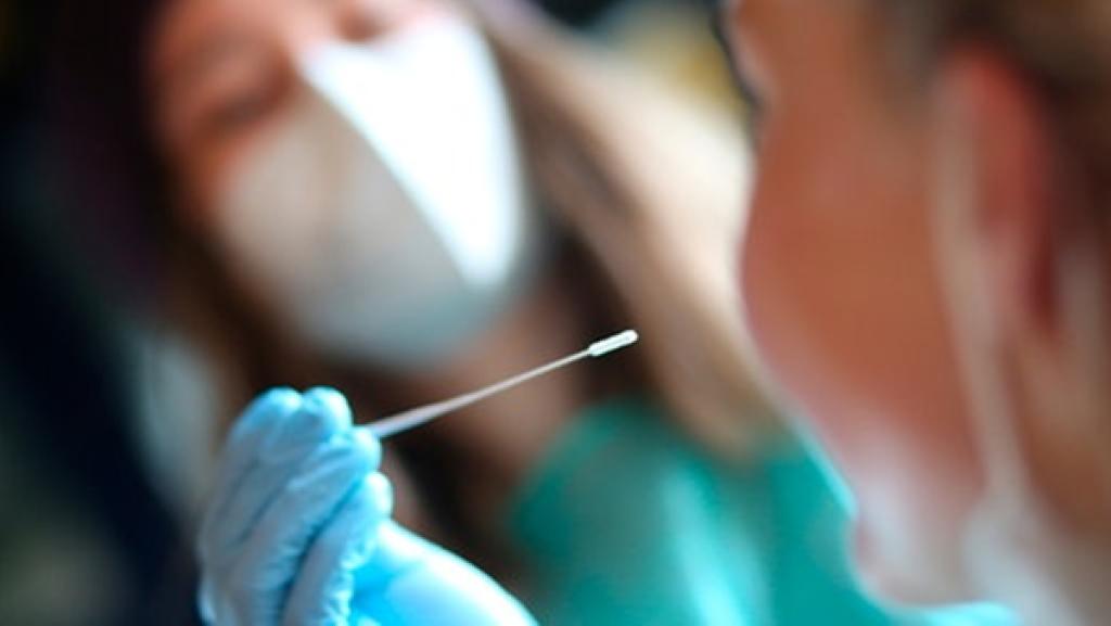 Hand hält Wattestäbchen vor Gesicht.