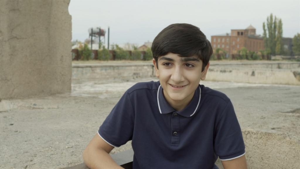 Rechte: hr/telekult Film und Medienproduktion GmbH Gor lächelnd vor Fabrikanlagen und einzelnen Bäumen.