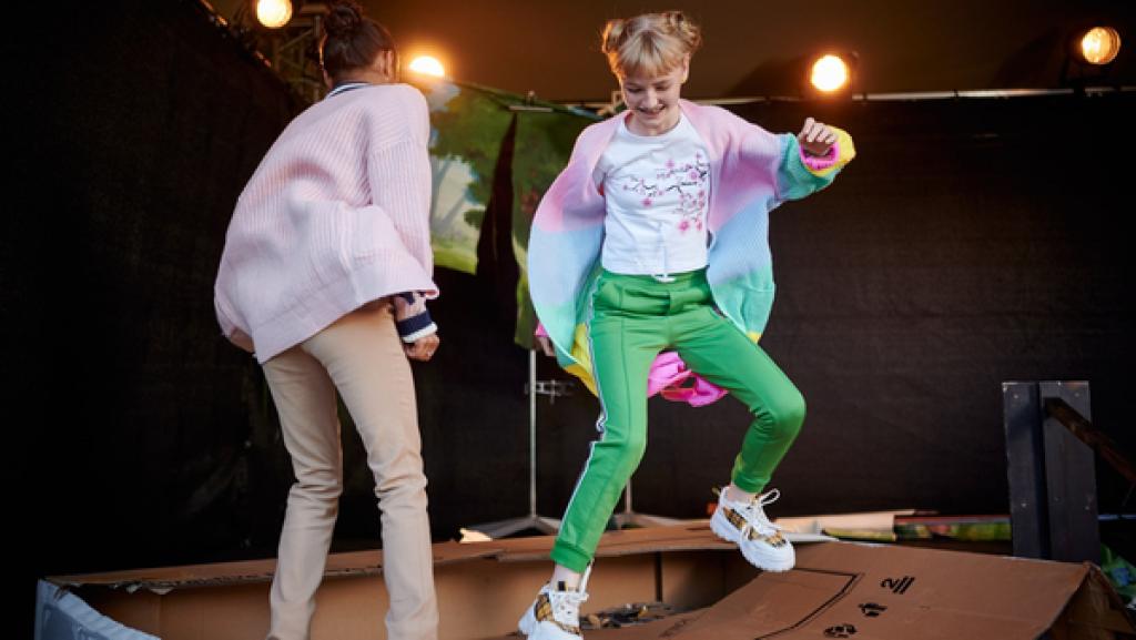 Zwei Mädchen springen auf einem großen Karton herum.