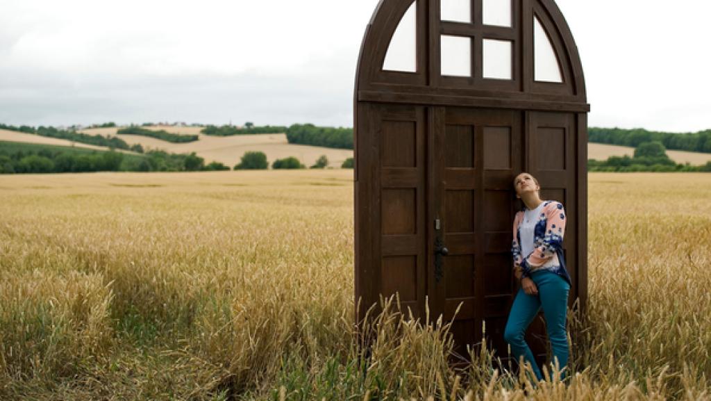 Mädchen lehnt an Holztür, die auf einem Feld steht.