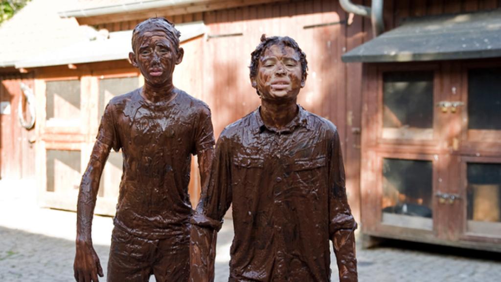 Zwei mit Schlamm bedeckte Jungs vor Kaninchenställen
