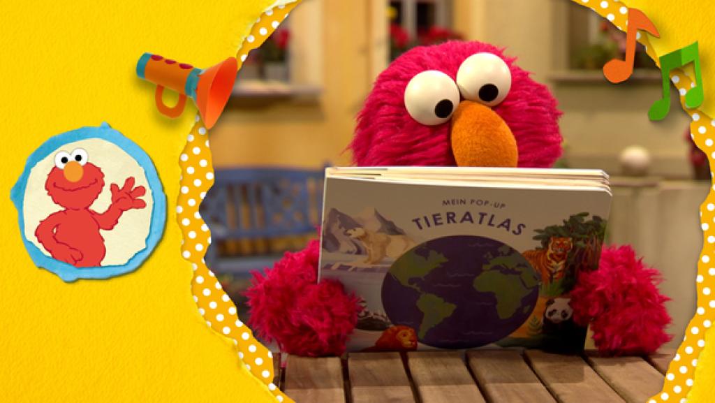 Elmo schaut sich einen Tieratlas an. 