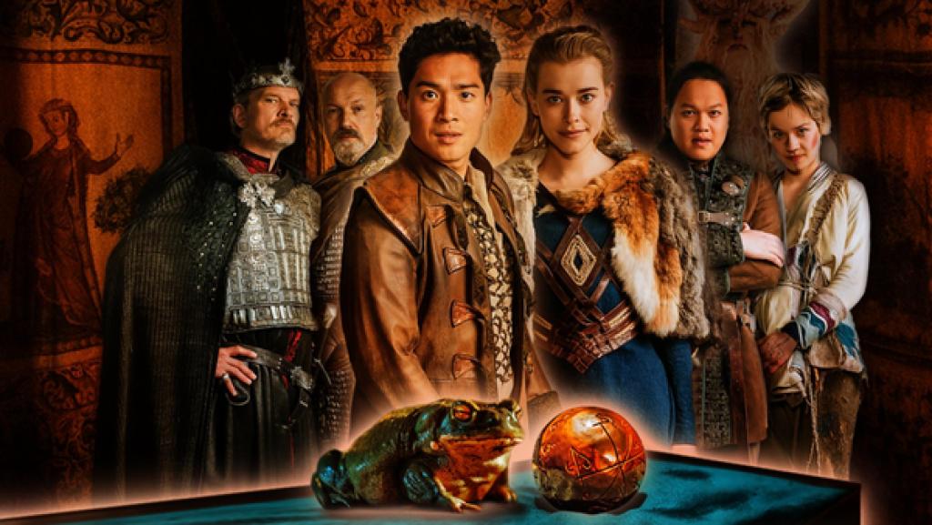 Das Märchen vom Frosch und der goldenen Kugel | Rechte: ZDF/Provobis Film GmbH/Jan Hromadko Sechs Personen in mittelalterlichen Gewändern schauen den Betrachter an. Von links: Neben einem groß gewachsenen älteren König, gespielt von Götz Otto, steht ein kräftiger Waffenmeister, gepielt von Simon Werner. Im Vordergrund in der Mitte präsentieren sich ein junger Prinz asiatischer Abstammung, verkörpert von Jan Liem, und eine blonde Prinzessin in einem blauen Kleid, dargestellt von Milena Tscharntke. Wieder etwas im Hintergrund sieht man einen jüngeren Mann mit schwarzen Haaren, gespielt von Anh Alexander Tran, und eine junge Frau mit kurzen blonden Haaren, verkörpert von Lea Drinda. Hinter ihnen sind braune bemalte Tücher gespannt. Ganz im Vordergrund sitzt ein Frosch neben einer goldenen Kugel.