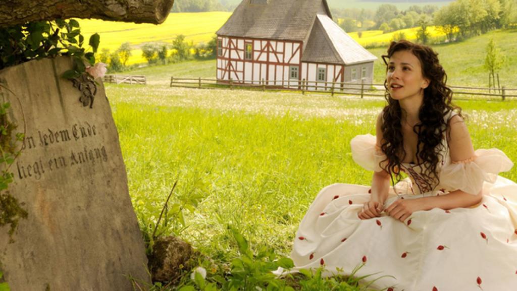 Ein Mädchen sitzt in einem weißen Kleid am Grab seiner Mutter