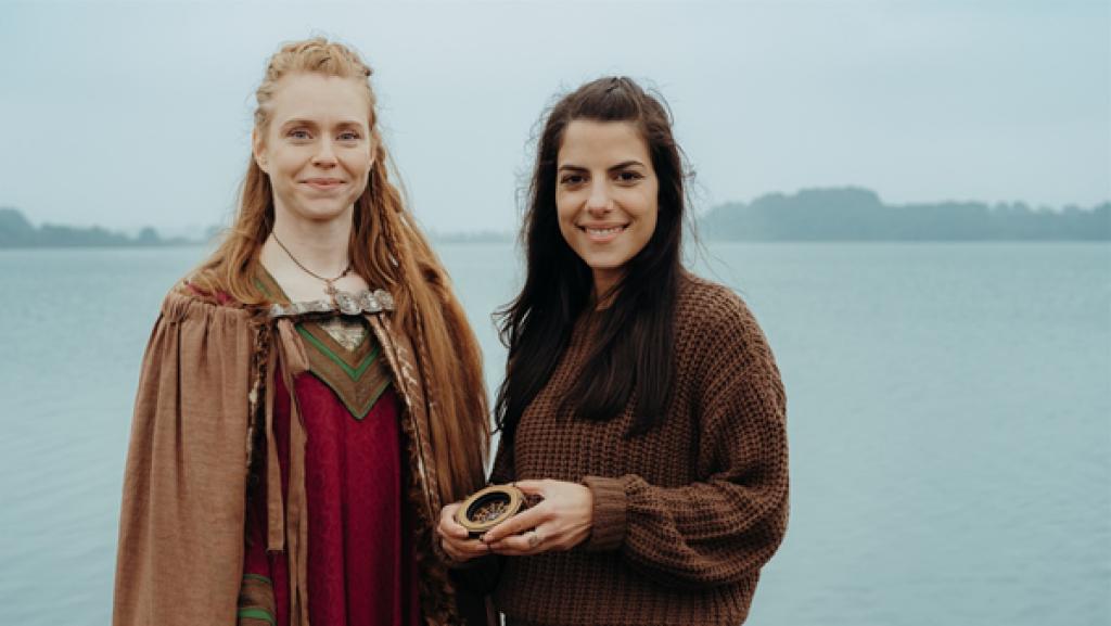 Rechte: ARD/hr/KiKA/Sabine Finger Clarissa trifft die Wikingerin Gudrid, die aus den Sagen bekannt ist. Sie stehen nebeneinander. Hinter ihnen ist das Wasser zu sehen.