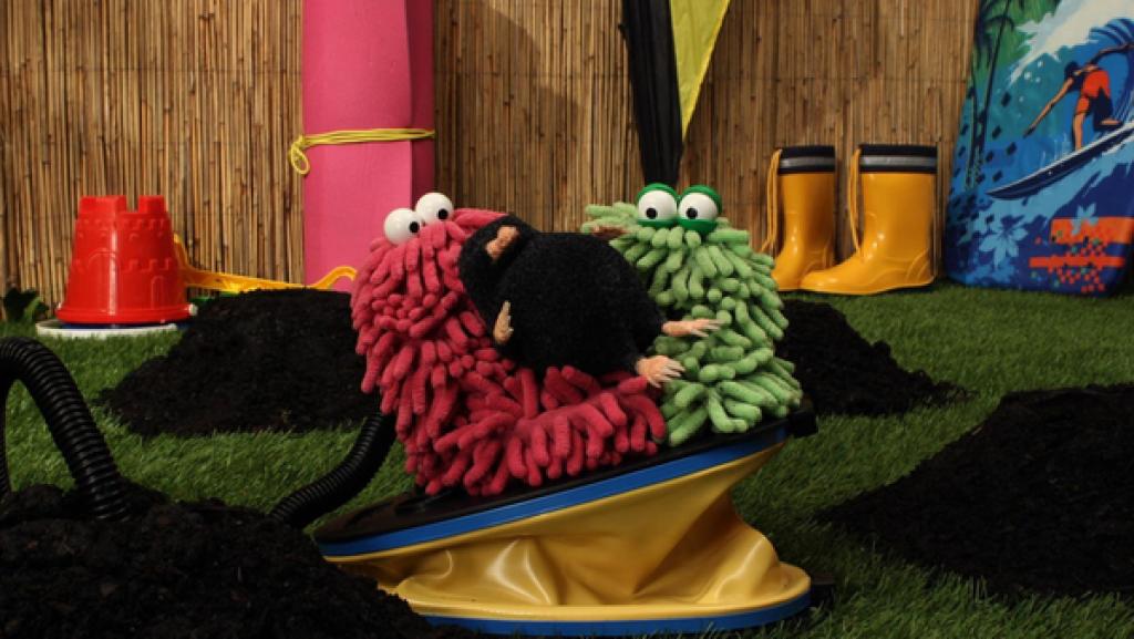 Wisch und Mop sitzen mit einem Maulwurf auf einem Blasebalg und schauen verdutzt